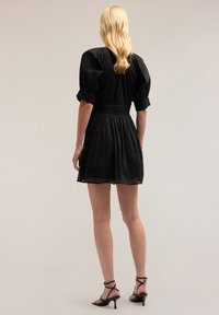 Schwarzes kurzes Kleid mit Puffärmeln, tailliertem Bund und plissiertem Rock. Durchsichtiger Stoff mit glatter Textur und subtiler Schattierung.