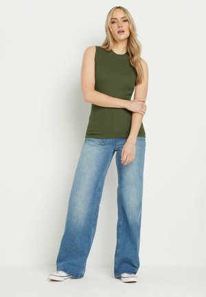 Olijfgroene geribbelde mouwloze top gecombineerd met lichtblauwe wijde jeans. De jeans hebben een klassiek vijf-pocket ontwerp en zijn iets beschadigd.
