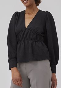 Black textured blouse with a deep V-neck, gathered waist, puffed long sleeves, and elasticized cuffs, paired with gray pants.