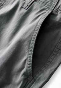 Grau gefärbte Stoffshorts mit glatter Textur, die über gestippte Nähte und eine seitliche Taschenöffnung verfügen. Einfaches Design ohne sichtbare Muster oder Akzente.