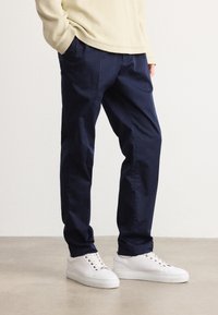 Marineblå bukser laget av lett stoff, med en avslappet passform og side lommer, kombinert med hvite sneakers.