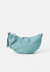 Tyrkysová taška Nike s texturovanou látkou, zakřiveným tvarem, nastavitelným popruhem a zapínáním na zip. Má malý stříbrný logotyp.