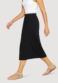 Gonna nera di lunghezza media con una texture liscia, abbinata a scarpe slip-on in rete di un leggero colore beige, caratterizzate da un design flessibile e accenti sottili.