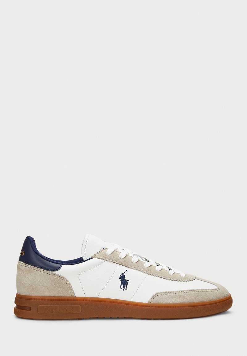 Zapatillas blancas y beige con un upper de ante y cuero, acentos en azul marino y suela de goma marrón. Presentan un logo en el lateral y diseño con cordones.