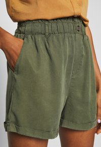 Olivgröna shorts i mjukt material, med elastisk midja, sidofickor och manschetter vid nederkanten, vilket ger en avslappnad passform.