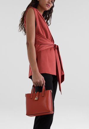 Red handbag made of structured leather with gold hardware, featuring double handles, sleek rectangular shape, and minimalistic design.