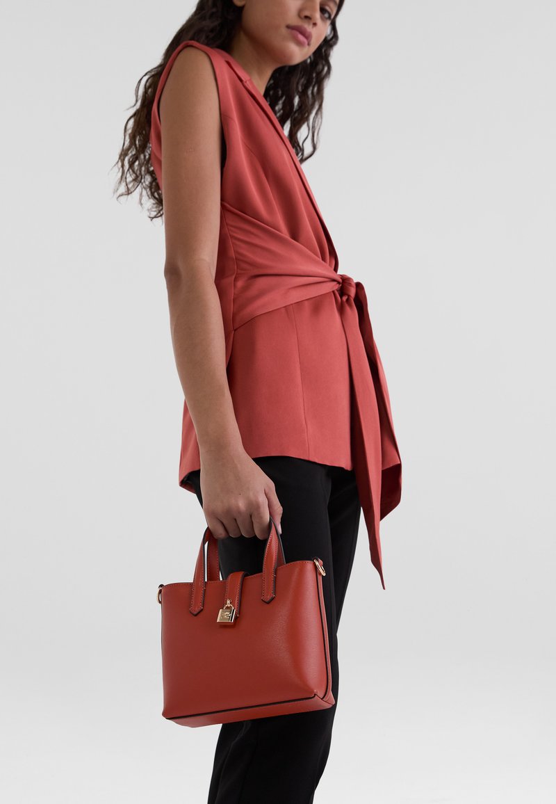 Red handbag made of structured leather with gold hardware, featuring double handles, sleek rectangular shape, and minimalistic design.