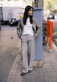 Pantalones grises claros a medida con cintura alta, combinados con una camiseta blanca y una chaqueta bomber beige. Zapatos de ante marrones completan el conjunto.