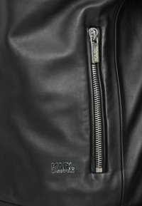 Jachetă din piele neagră cu un design eleganță, fermoar proeminent cu elemente de metal argintii și logo-ul brandului "KARL LAGERFELD" pe lateral.