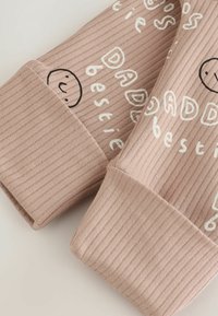 Jasnoróżowa dzianina prążkowana z zabawnym napisem i uśmiechniętą twarzą. Rękawy są grube, a projekt zawiera napisy "DAD" i "najlepszy przyjaciel" w białym kolorze.