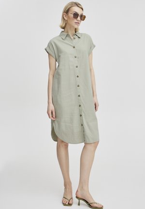 Hellolivgrünes Hemdblusenkleid mit Kragen und kurzen Ärmeln, das eine gerade Passform, abgerundeten Saum und Holzkneippdetails aufweist.