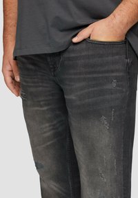 Jean en denim noir délavé avec des détails effilochés et des poches, associé à un t-shirt gris ample. Texture douce et style décontracté.