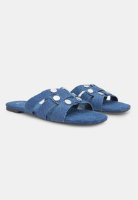 Sandales en denim à semelle plate, avec plusieurs lanières diagonales et des accents ronds en argent pour plus de détails.