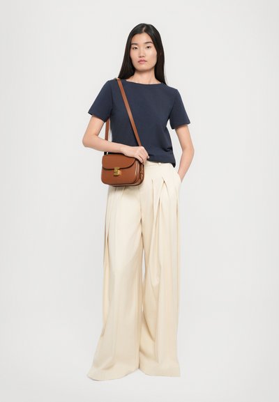 Maglietta navy a maniche corte, pantaloni a gamba larga plissettati color crema e una borsa a tracolla marrone con dettaglio della chiusura dorata. Design e colori semplici e puliti.