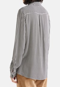 Svart och vit houndstoothskjorta med button-down-krage, långa ärmar och slitsar på sidorna av muddarna. Mjuk tyg med en strukturerad yta.