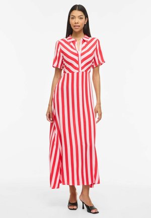 Kvinde, der står iført en rød- og hvidstribet kjole til anklerne med korte ærmer og sorte åbne højhælede sko.