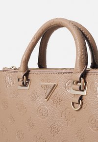 Beżowa torebka o teksturowanej powierzchni ze złotymi akcentami, z wytłoczonymi wzorami logo, podwójnymi uchwytami i zamknięciem na zamek u góry.