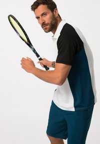 Joueur de tennis portant un polo noir et blanc avec des accents turquoise, tenant une raquette. Le tissu semble respirant, idéal pour le sport.