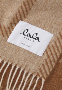 Cachecol de lã em tons de bege e castanho com franjas, e uma etiqueta branca com a inscrição "lala BERLIN made in italy" costurada no tecido.