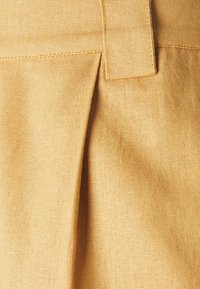 Light yellow linen fabric with a textured finish, featuring a pleat detail and a stitched waistband for added structure.