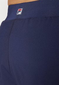 Tamsiai mėlynos sportinės šortai su lygiu paviršiumi, turintys platų elastingą juosmenį ir mažą logotipą viršutinėje nugaros dalyje.