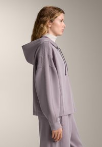 Felpa con cappuccio in lavanda con dettagli a coste, vestibilità morbida, cappuccio con cordini e texture morbida, abbinata a pantaloni coordinati.