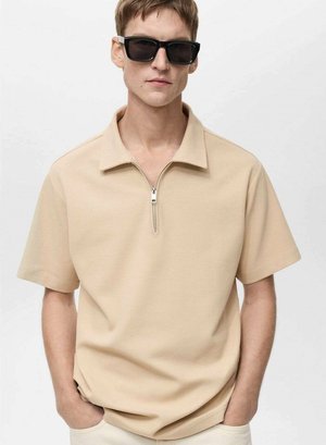 Beige Poloshirt mit kurzem Reißverschluss, kurzen Ärmeln und einem strukturierten Stoff. Kombiniert mit schwarzen Sonnenbrillen für einen modernen Look.