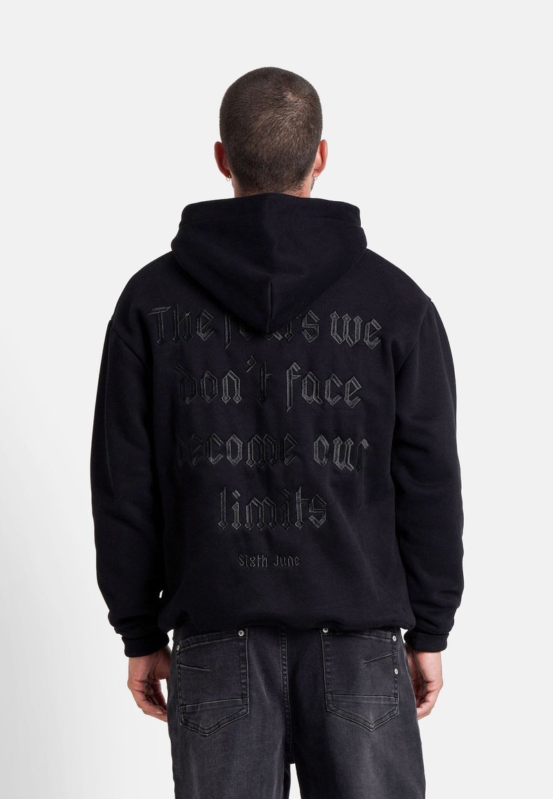 Felpa nera con cappuccio e una grande scritta testurizzata sul retro. Presenta un cappuccio con lacci e polsini a costine. Design semplice, vestibilità casual.