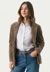 Brun kordfløjl blazer med notched lapels, båret over en hvid skjorte, parret med højtaljede blå denim jeans og et tanfarvet bælte.