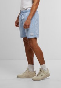 Shorts de bain bleu clair avec une finition texturée, taille élastique et poche latérale, arborant un petit logo KANI sur l'ourlet inférieur.
