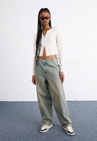 White ribbed cropped long-sleeve top, high-waisted light blue wide-leg jeans, and green-trimmed sneakers. Smooth texture, fitted design.