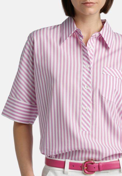 Roze en witte gestreepte shirt met kraag, korte mouwen, knopen aan de voorkant en een zak. Draagt een roze riem over witte broek.