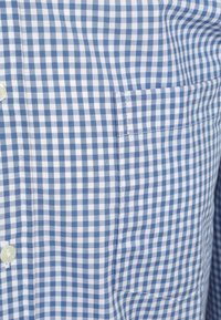 Blauw-wit geblokt overhemd met knoopsluiting, opgeschoven kraag en een enkele borstzak aan de linkerkant.