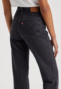 Pantalones vaqueros negros de mezclilla con cintura alta, con un diseño clásico de cinco bolsillos, textura descolorida y una parche de cuero marr�ón claro en la parte trasera de la cintura.