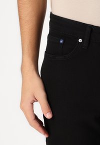 Črne jeans hlače s slim fit krojem, okrašene z modrimi in srebrnimi gumbi, petimi žepi in vidnimi šivi.