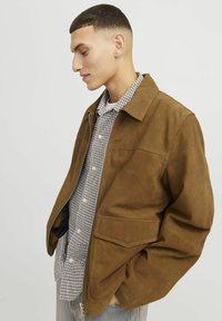 Brown suede jacket with a zip front, large patch pockets, and a classic collar, layered over a black and white checkered shirt.