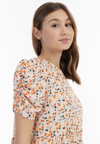 Blumenkleid mit Puffärmeln, das eine rosa Basis hat, die mit orangefarbenen und schwarzen Blumen, grünen Blättern und subtilen dekorativen Akzenten verziert ist.