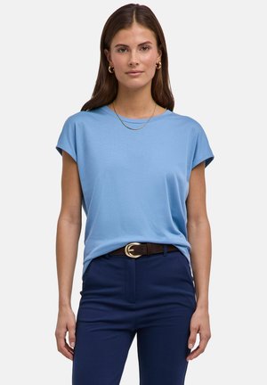 Hellblaues T-Shirt mit kurzen Ärmeln aus weichem Stoff, ausgestattet mit einem klassischen Rundhalsausschnitt und einem entspannten Schnitt. Das Modell trägt marineblaue Hosen und einen braunen Gürtel.