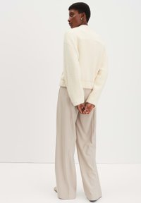 Crèmekleurige trui met een gebreide textuur en een cropped fit, gecombineerd met lichtbeige wijde broek. Het ontwerp heeft lange mouwen en een ronde hals.