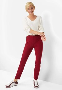 Red tapered pants paired with a ribbed cream sweater, featuring a v-neck and rolled sleeves. Worn with white and burgundy sneakers.
