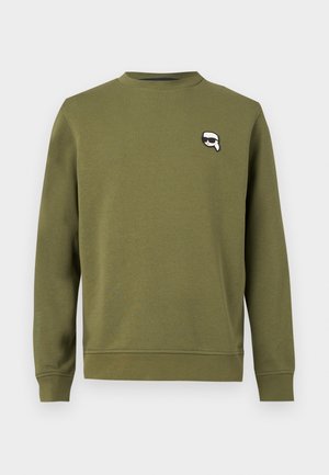 Φούτερ με μακριά μανίκια σε πράσινο ελιάς με στρογγυλή λαιμόκοψη και μικρό ασπρόμαυρο λογότυπο με πρόσωπο που φορά γυαλιά ηλίου στο επάνω αριστερό μέρος του στήθους.