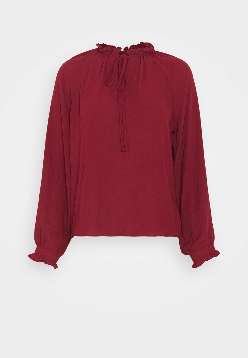 Blouse bordeaux à manches longues avec col et poignets volantés, dotée d'un lien à nouer au niveau de l'encolure et d'une coupe ample.
