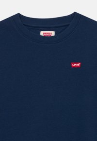 Sweat-shirt bleu marine avec un col côtelé, arborant une petite étiquette rouge Levi's sur la poitrine, fabriqué à partir d'un tissu doux et texturé.