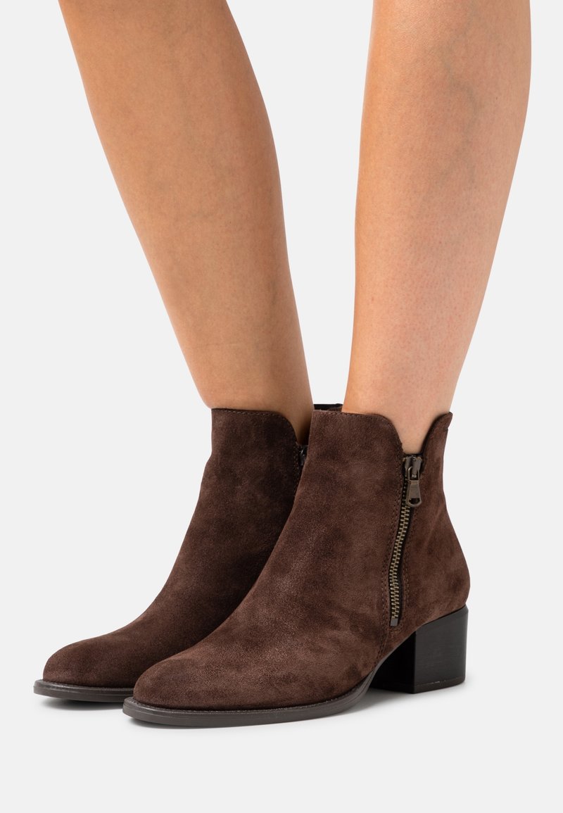 Bottines en suédine marron avec un bout rond et une fermeture éclair sur le côté, dotées d'un talon empilé et d'une texture lisse.