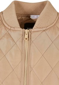 Quiltad beige bomberjacka med ribbad krage, hel dragkedja framtill och slät textur med diagonalt stickmönster.