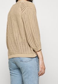 Suéter beige de punto con un diseño suelto y perforado y puños acanalados. El dobladillo inferior es sencillo, combinado con vaqueros de color azul claro.