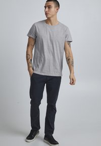 Grå kortermet t-skjorte med rund hals, kombinert med mørk marineblå bukser og svarte joggesko. Minimalt design, avslappet passform, glatt tekstur.