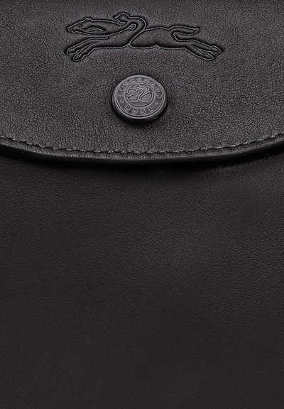 Schwarze Ledertasche mit einem Klappdeckel, der ein geprägt laufendes Pferde-Logo und einen runden Knopf mit dem Text "LONGCHAMP 1948" zeigt.