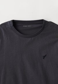 Ναυτ�ικό μπλε βαμβακερό t-shirt με στρογγυλή λαιμόκοψη και κοντά μανίκια, φέρει ένα μικρό μαύρο κεντητό λογότυπο πουλιού στο αριστερό στήθος.