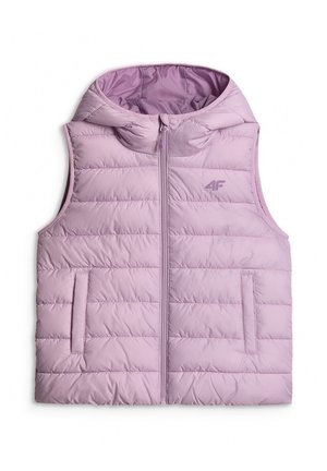 Młoda dziewczyna ubrana w fioletową pikowaną kamizelkę, różowo-fioletową bluzę tie-dye, fioletowe spodnie, białą opaskę na głowę oraz białe trampki, stojąca na tle szarego tła.